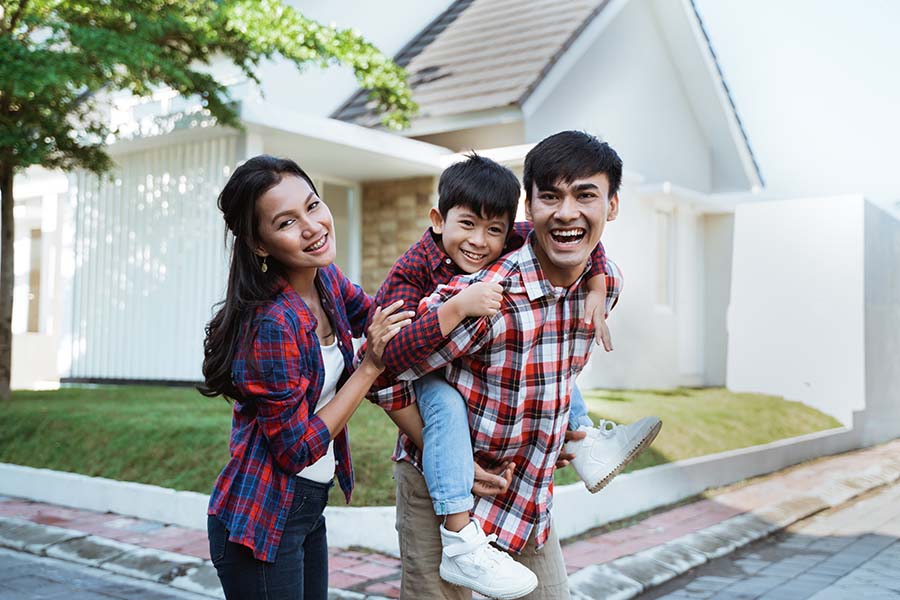 Personal Insurance - Happy Young Family Standing Outside Their Home On Sunny Day
