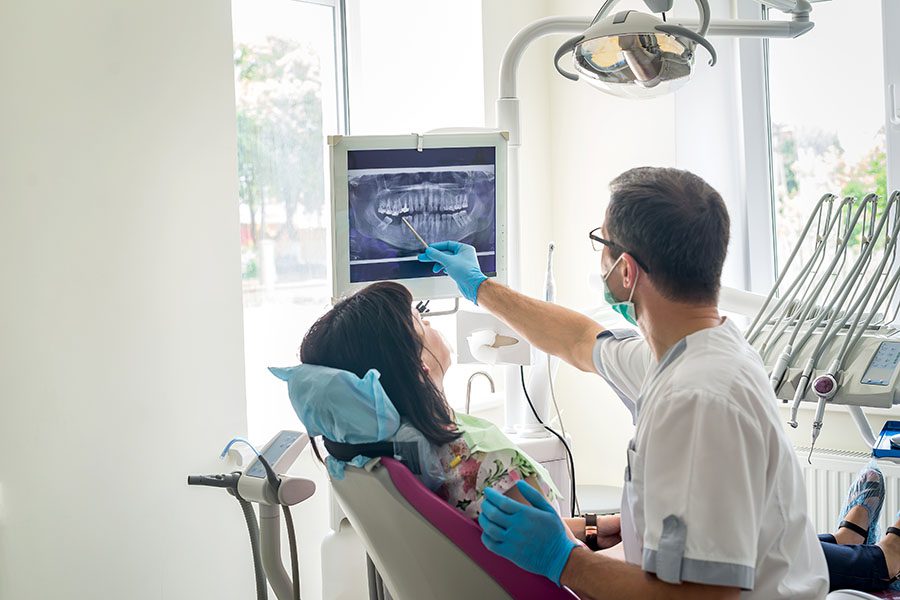 Specialized Business Insurance - Dentist In Office Showing His Patient An Xray Of Her Teeth